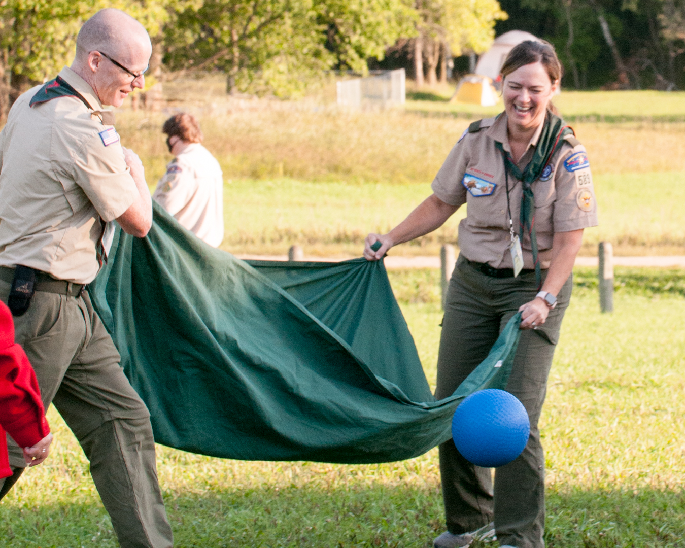 Two older adult participants wearing the Scout uniform are playing a team-building game and laughing.